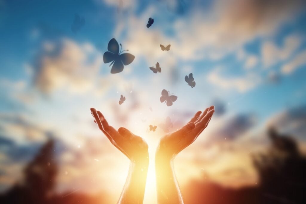 Hands releasing flock of butterflies into the sky symbolizing hope