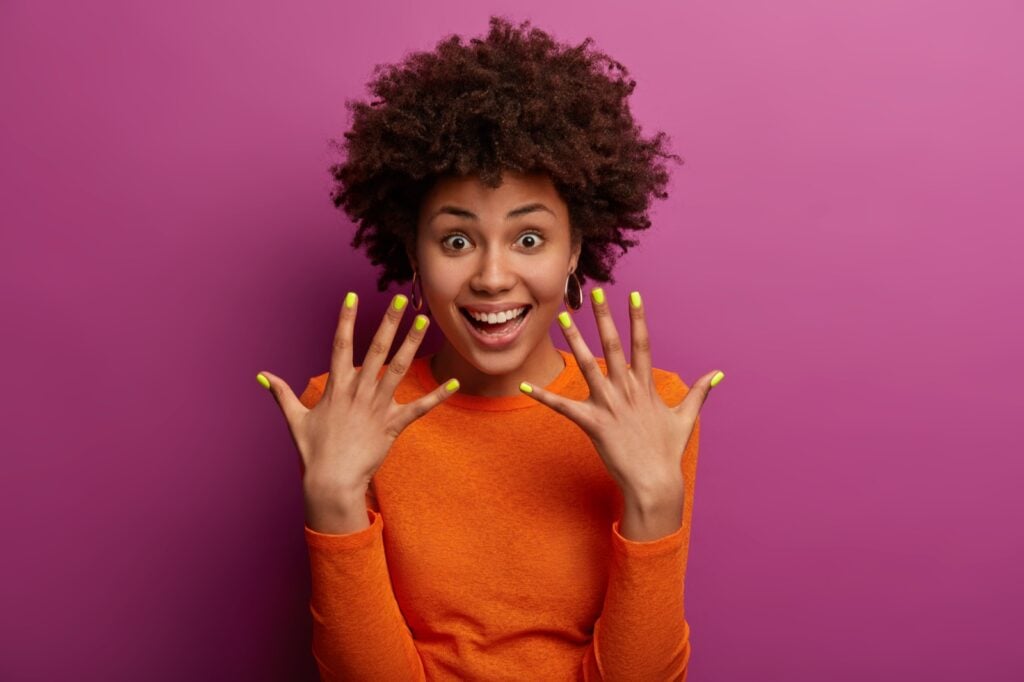 Happy curly haired woman showing manicured yellow nails