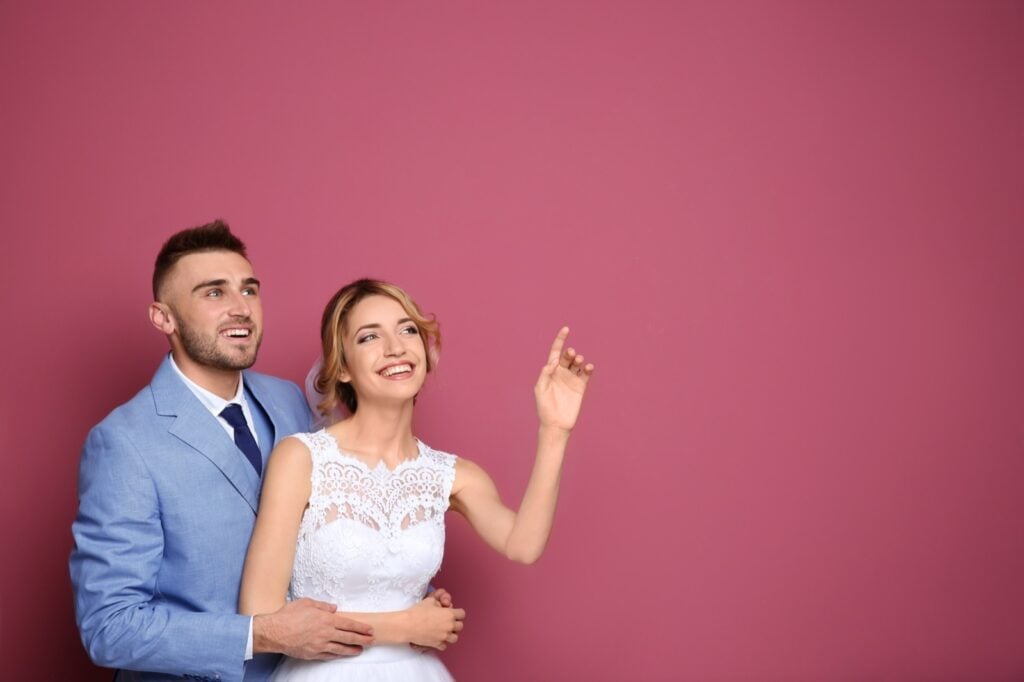 Happy wedding couple pointing on color background