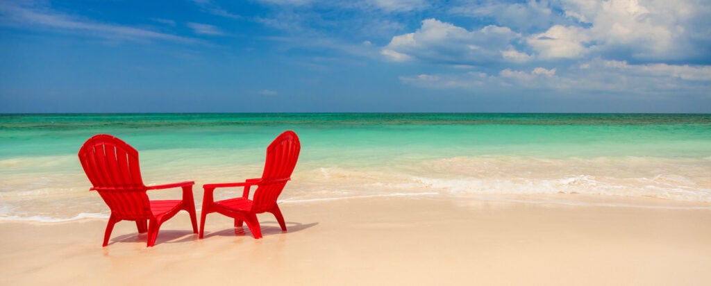 Red chairs on the beach next to turquoise water.