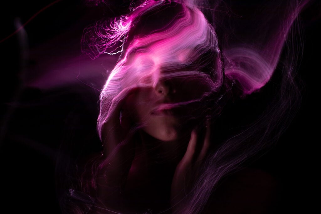 Close up of woman's face on a black background with magenta color swirling around her face.