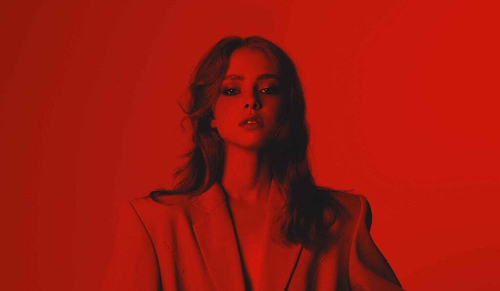Close up of woman in a suit standing in a complete red light to represent the red aura.