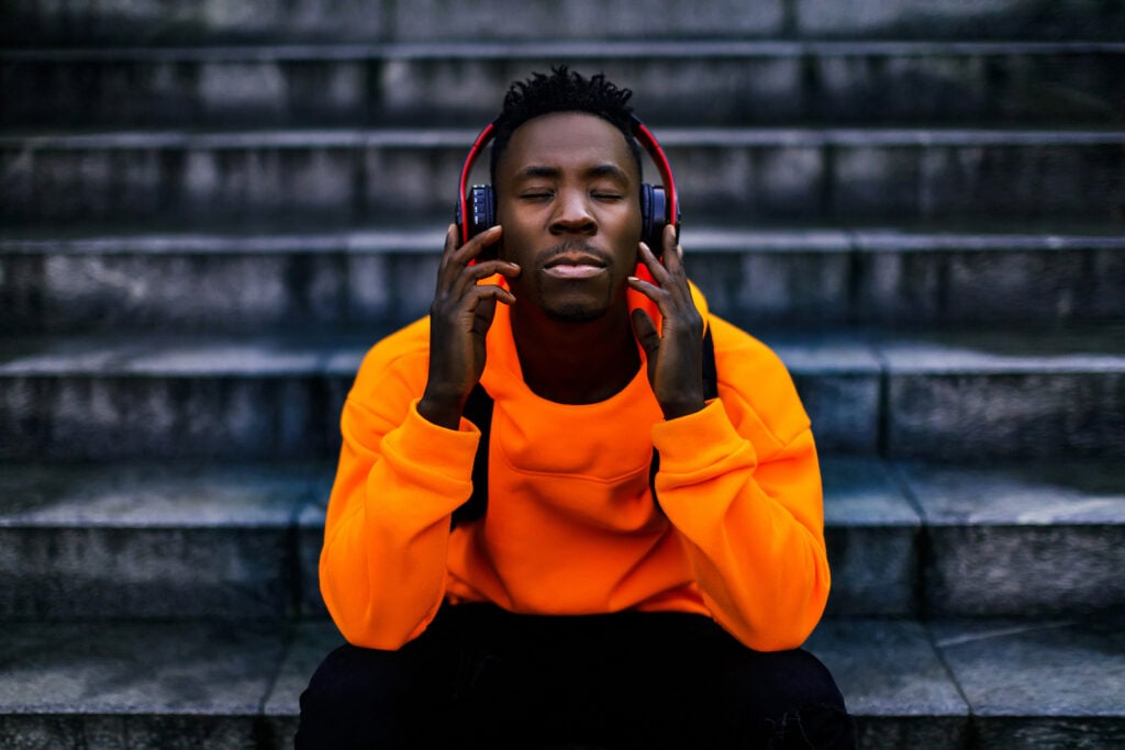 Close up of a man in a bright orange hoodie with wireless headphones listening to music.