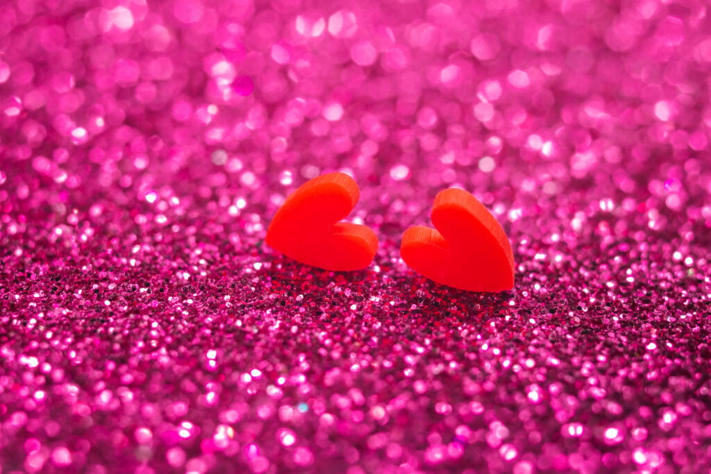 Close up of magenta glitter with two small red hearts standing beside each other.