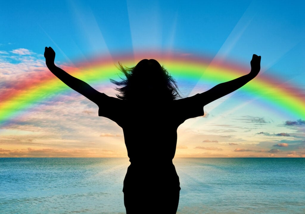 Silhouette of a woman with raised arms at the ocean with rainbow colors
