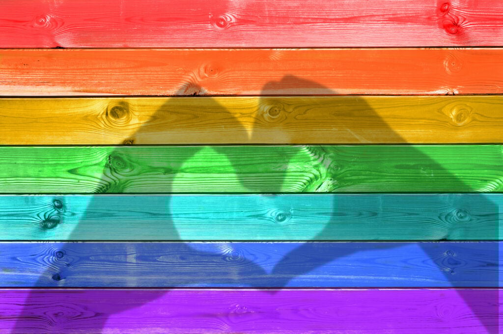 Shadows of hands forming a heart on rainbow painted wood planks.