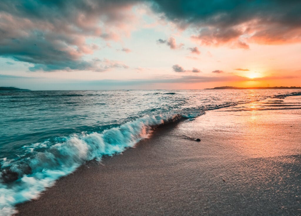 Waves rolling in on the beach with the sunset in the background.
