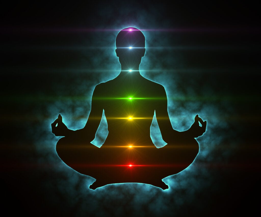 Silhouette of meditating figure with glowing teal aura and the seven chakras.