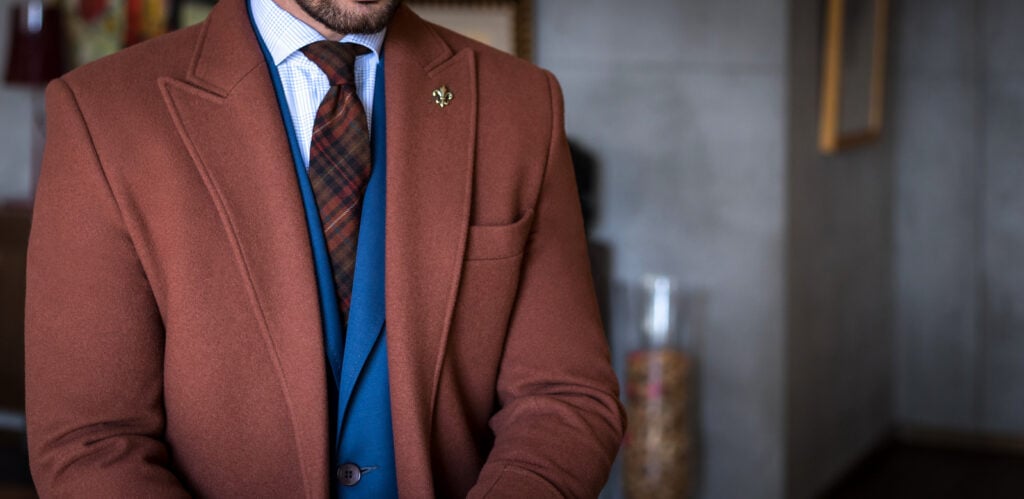 Man in custom tailored suit and trench coat posing indoors.