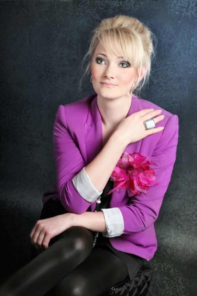 Portrait of woman with purple jacket against black background.