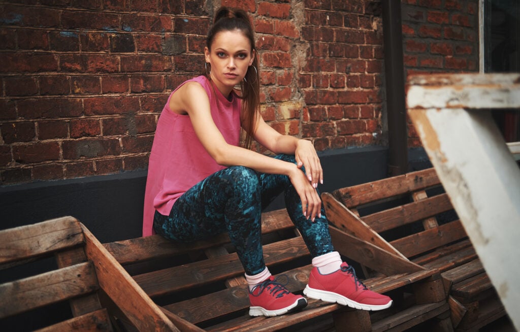 Woman sitting on bench with a pink shirt and red shoes.