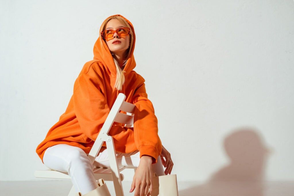 Girl wearing orange hoodie and glasses posing on white background.