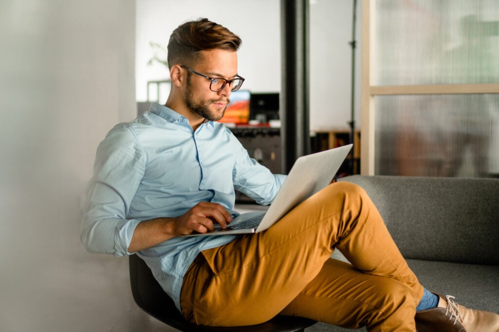 Young man typing on laptop with pastel blue shirt.