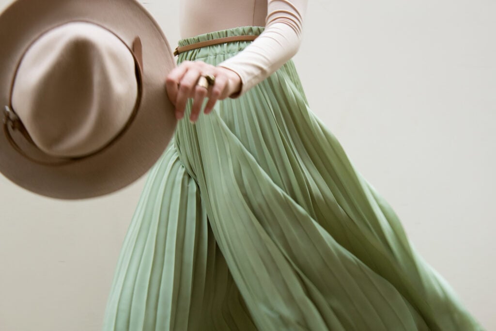 Hat, beige blouse, and turquoise skirt on light background.