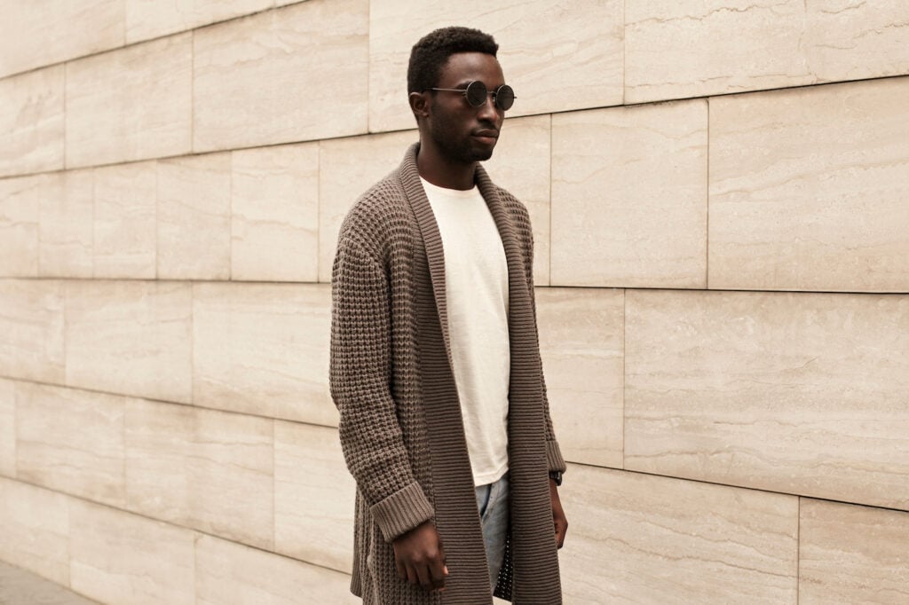 Stylish man wearing brown knitted cardigan, and sunglasses on city street.