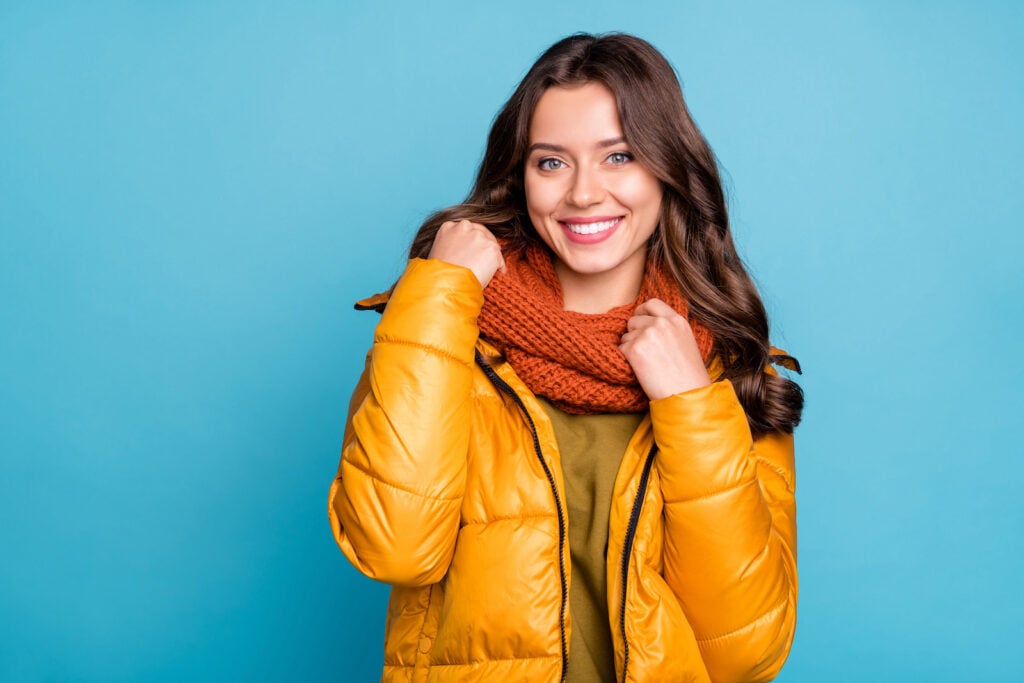 Woman holding knitted scarf with blue background.