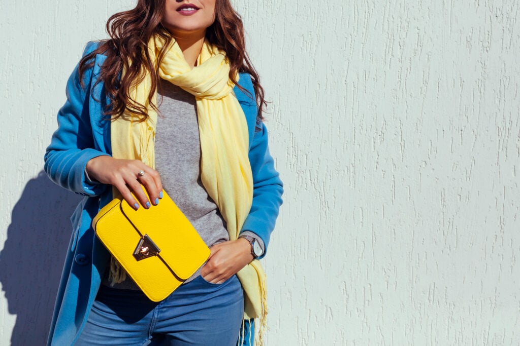 Young woman holding stylish yellow handbag and wearing a trendy blue coat.