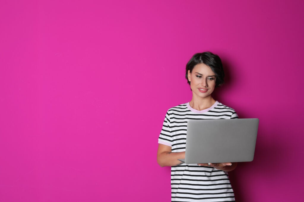 Woman with a laptop standing next to a magenta wall