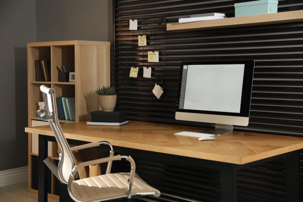 Comfortable workplace with office chair and computer against black wall.