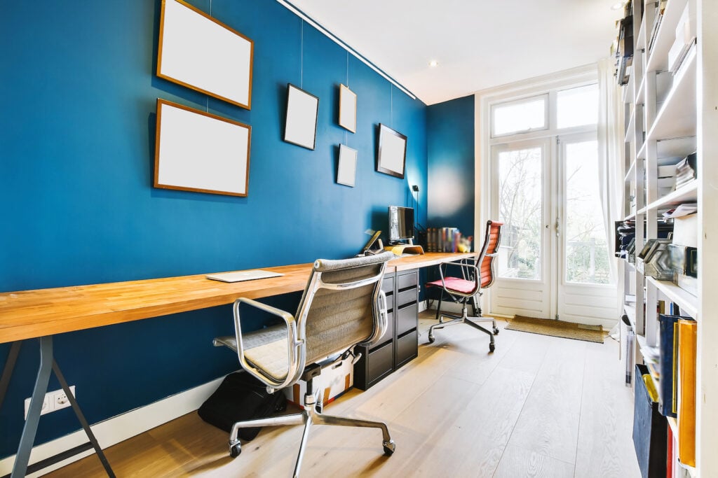 Room with blue walls and wooden table with computer and chairs in home office.