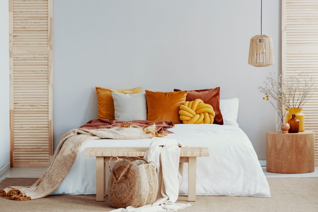 Wooden bench in front of king size bed with burnt orange pillows.