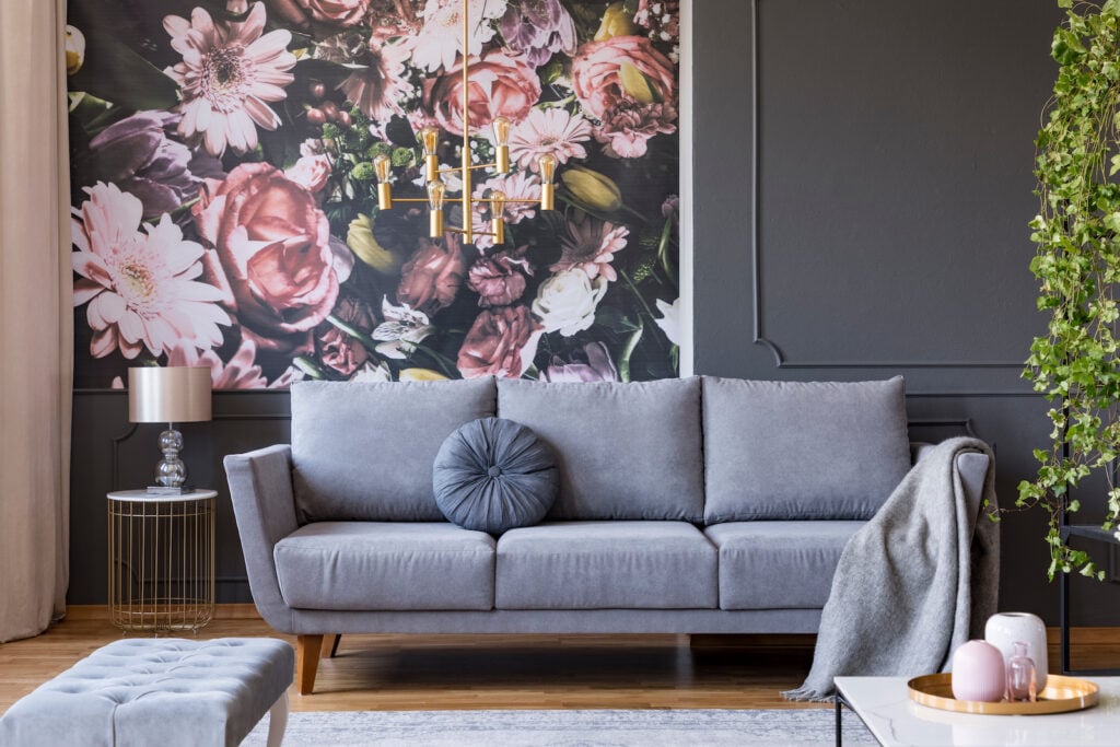 Grey couch in living room with flower wallpaper and lamp on table.