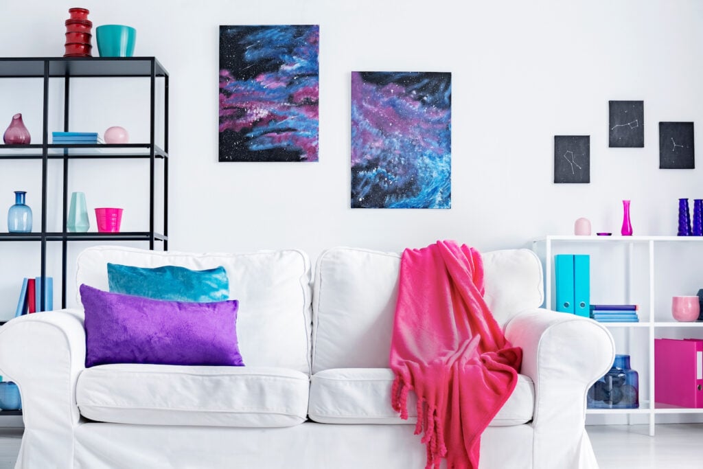 Closeup of white comfortable couch with pink blanket and purple and blue pillows.