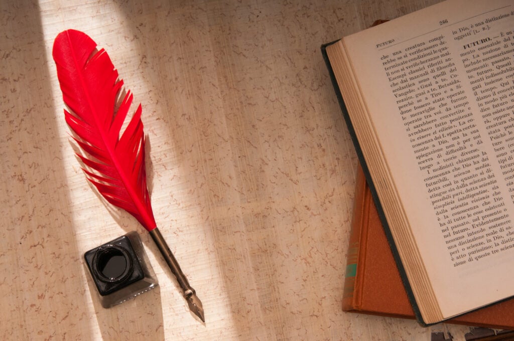 Red quill pen and black inkwell on a papyrus sheet.