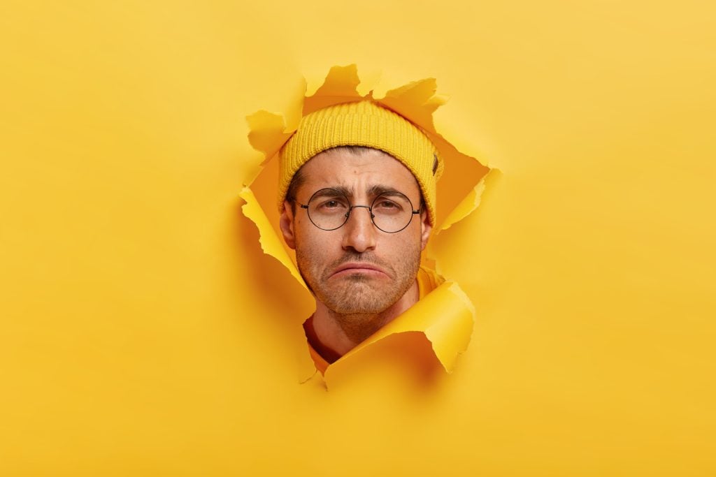 Sad man in yellow hat looks out from ripped yellow background