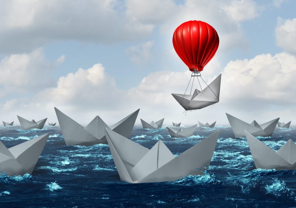 A red hot air balloon lifts a paper boat above the rest