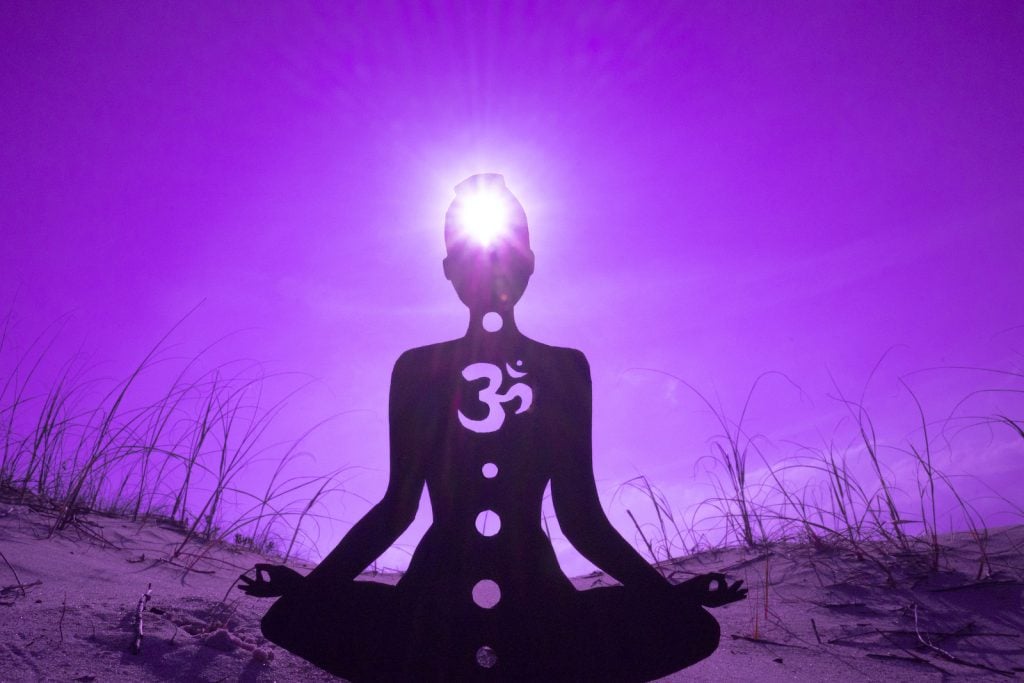 A silhouetted person does yoga on a sand dune under a purple sky