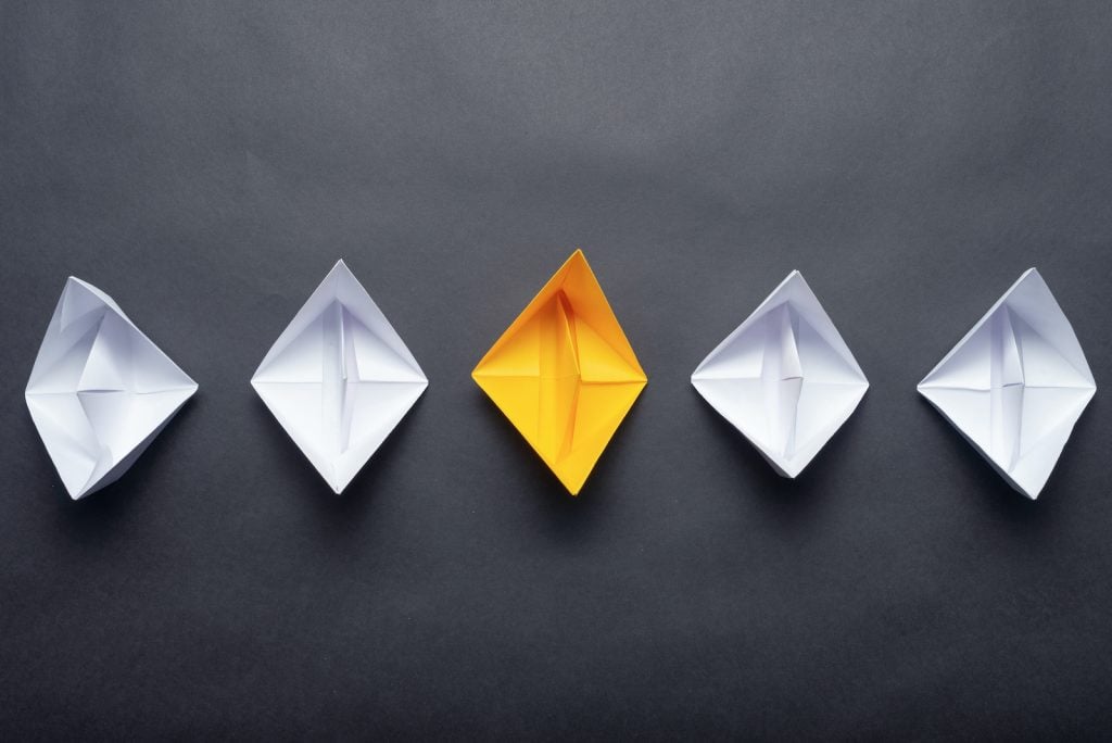 A row of white origami boats with a yellow one that stands out