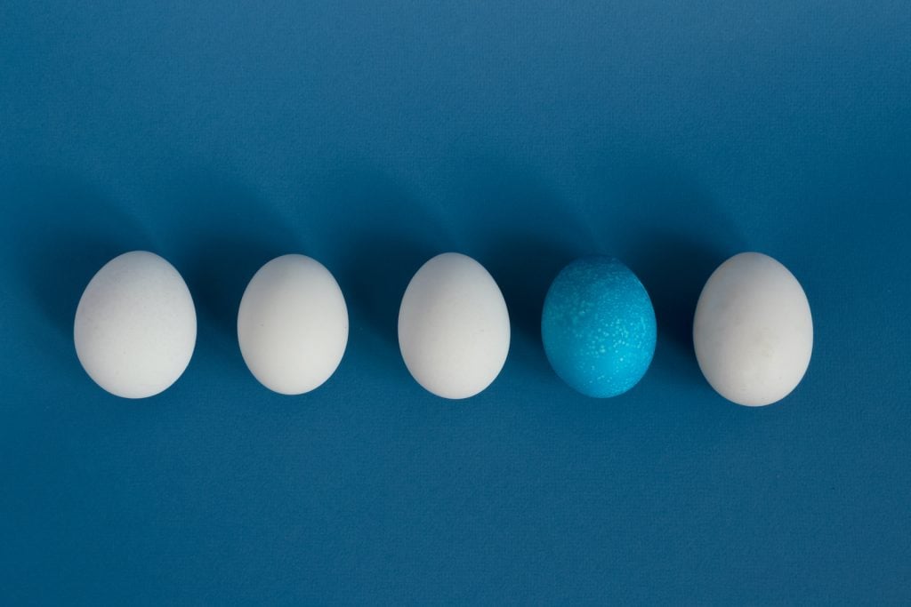 A blue egg in a row of white eggs on a blue background
