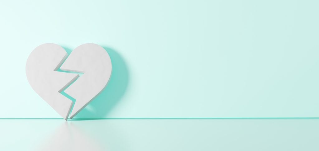 A broken white heart leans on a light green background