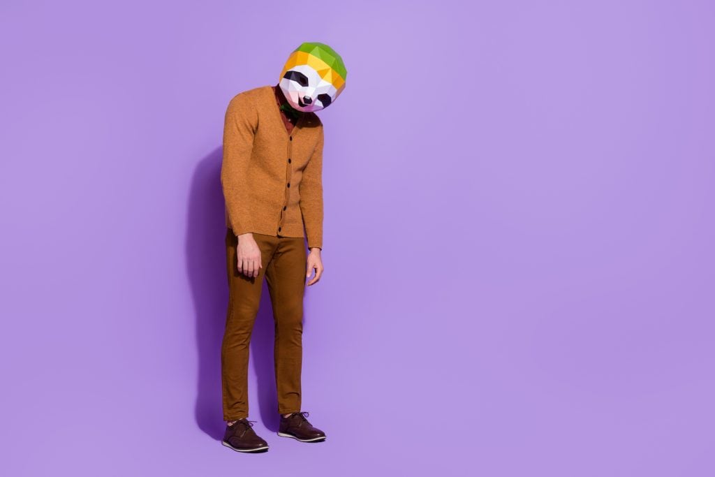 A disappointed person dressed in brown and wearing a mask stands in front of a lavender background