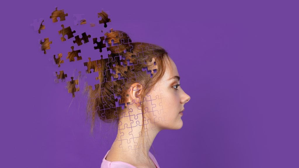 A conceptual photo of puzzle pieces making up a young woman's face on purple background