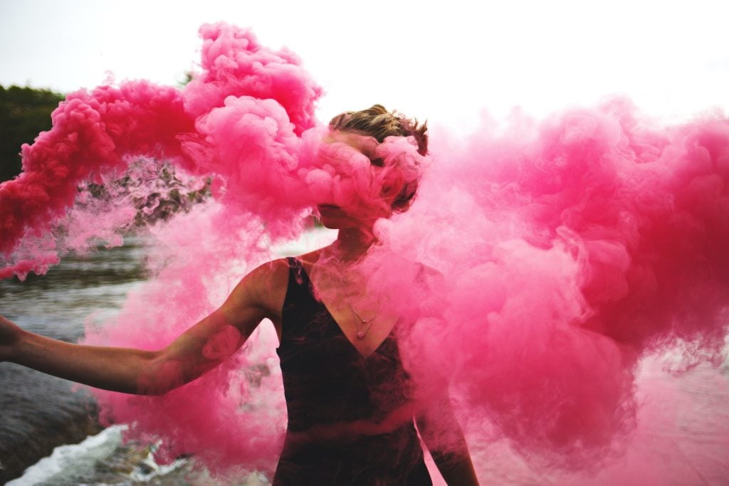 A woman outside surrounded by hot pink smoke