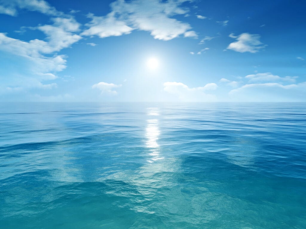 A white sun in a blue sky above tropical ocean water