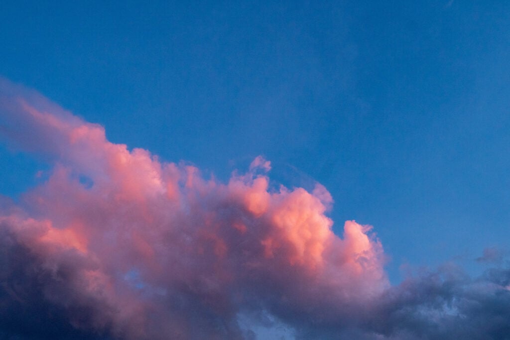 Fluffy pink-tinted clouds float across a bright blue sky