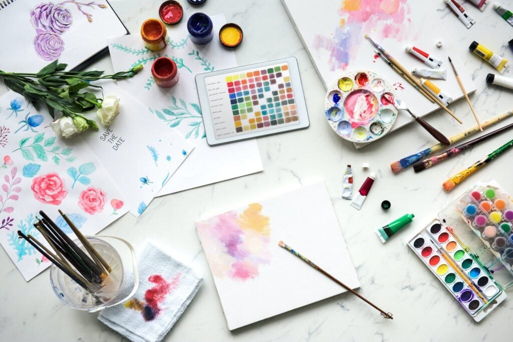 A busy artist's desk shows different paints being mixed in order to match a set of color swatches