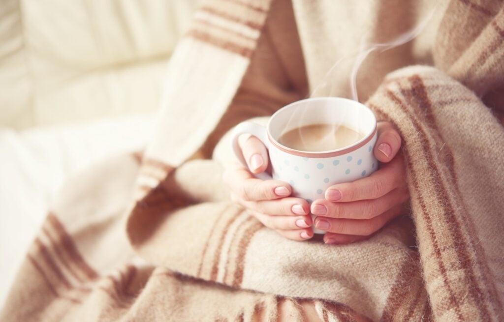 Person holding coffee while wearing warm blanket