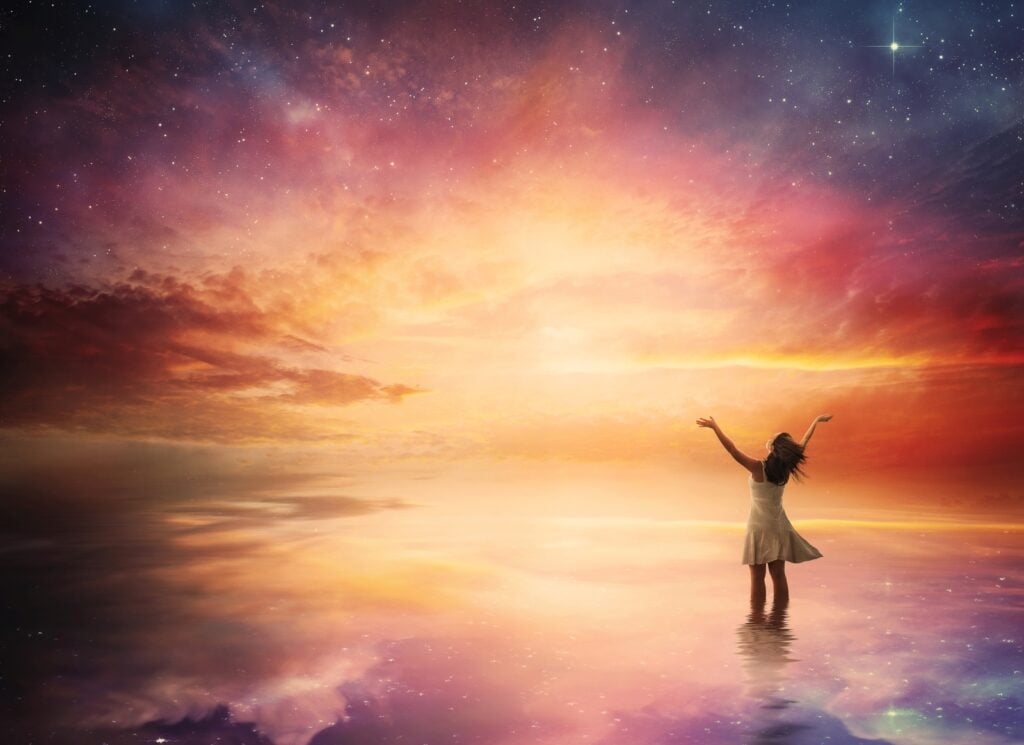 Woman surrounded by colorful sky and water