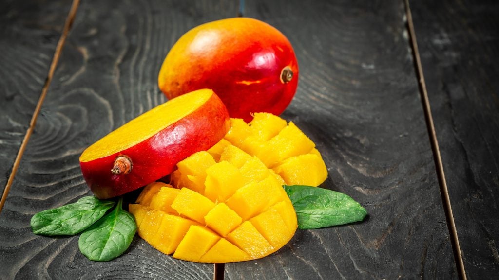 Fresh and beautiful whole mango fruit with another one sliced and diced mango chunks on a black wooden background