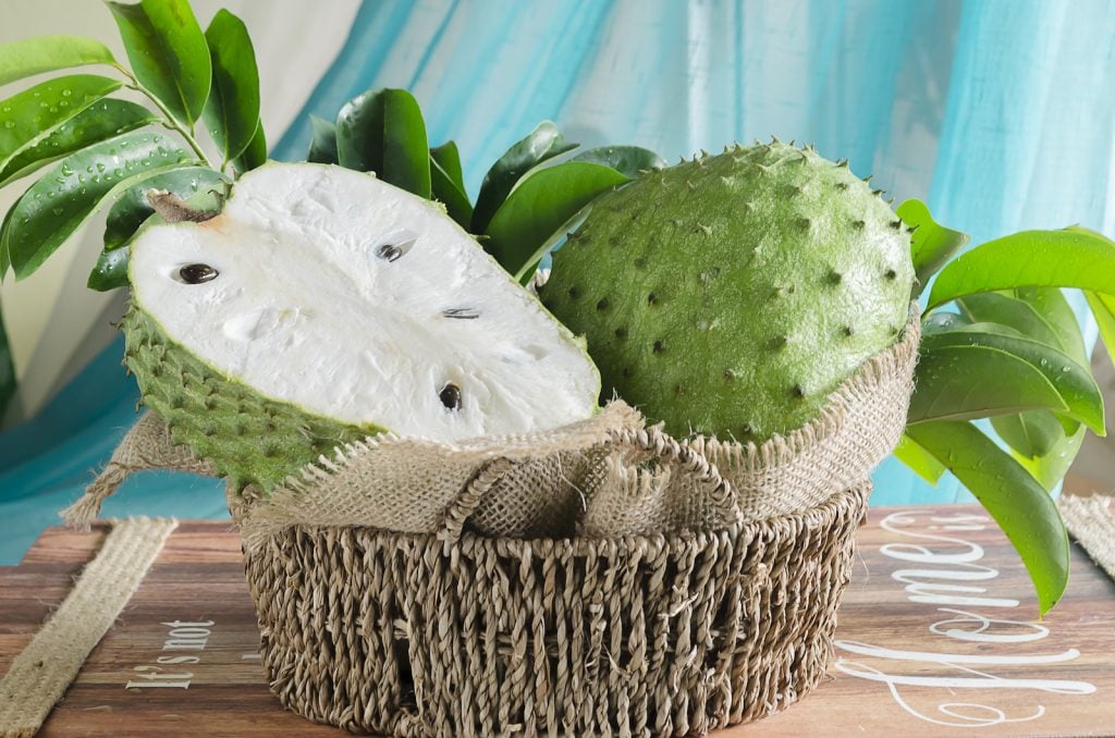 Soursop fruit in a woven basket on a wooden crate with blue background