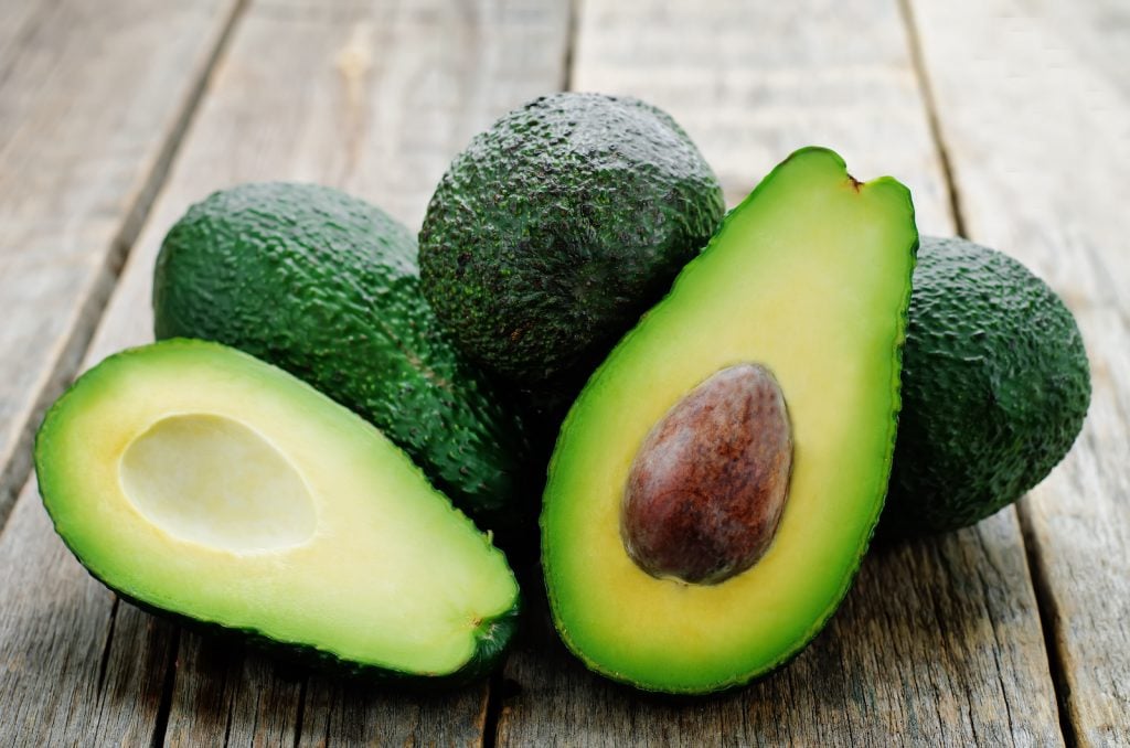 Fresh green avocado on a dark rustic wooden table