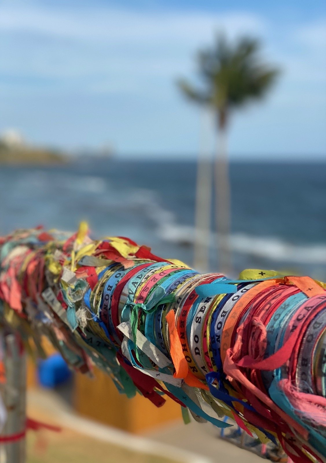 Several Bahia Bands tied around a pole with a blurred coconut tree and the ocean in the background