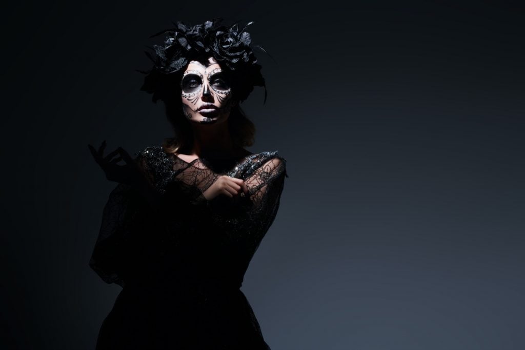 Beautiful woman in a dark room wearing black clothes and makeup celebrating Day of the Dead