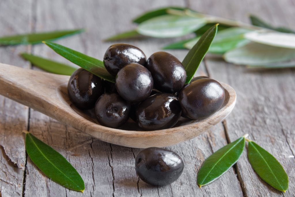 Black olives on a wooden spoon with leaves around