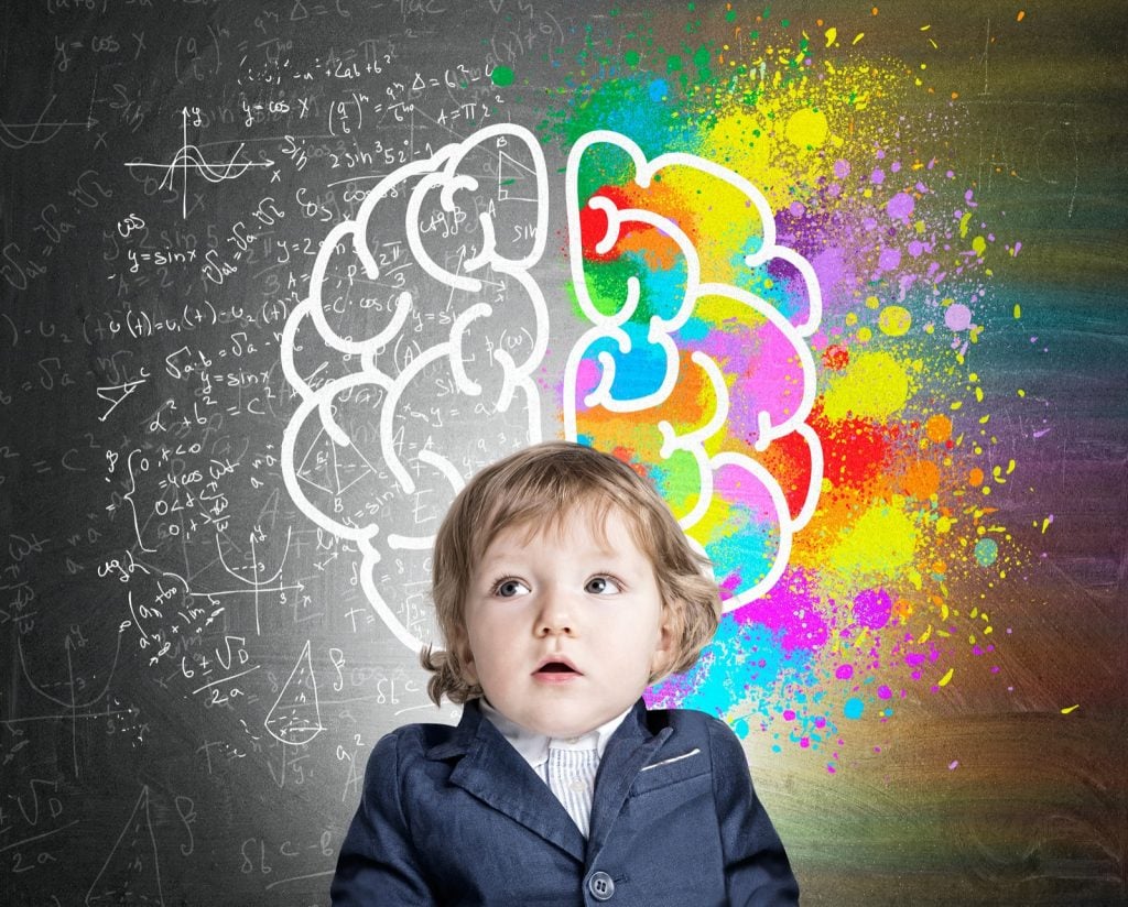 Portrait of boy wearing a suit and standing near a chalkboard with a colorful brain illustrating a kids development