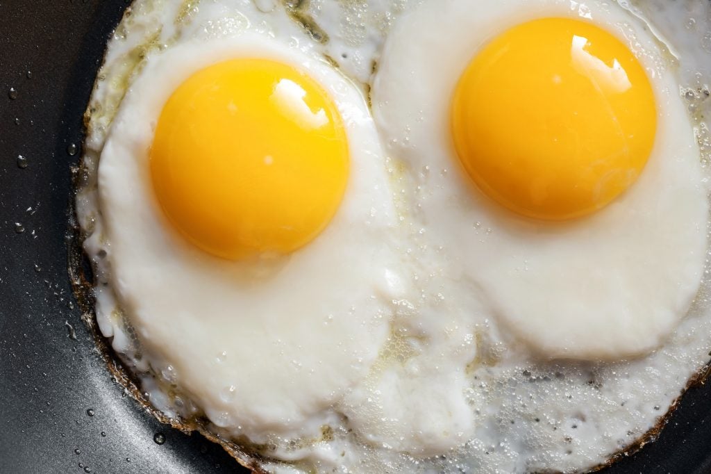 Two fried eggs with bright yellow yolks in a black frying pan